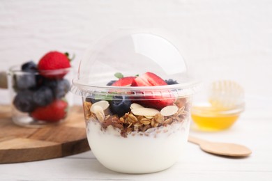 Photo of Tasty granola with berries, yogurt and almond flakes in plastic cup on white table, closeup