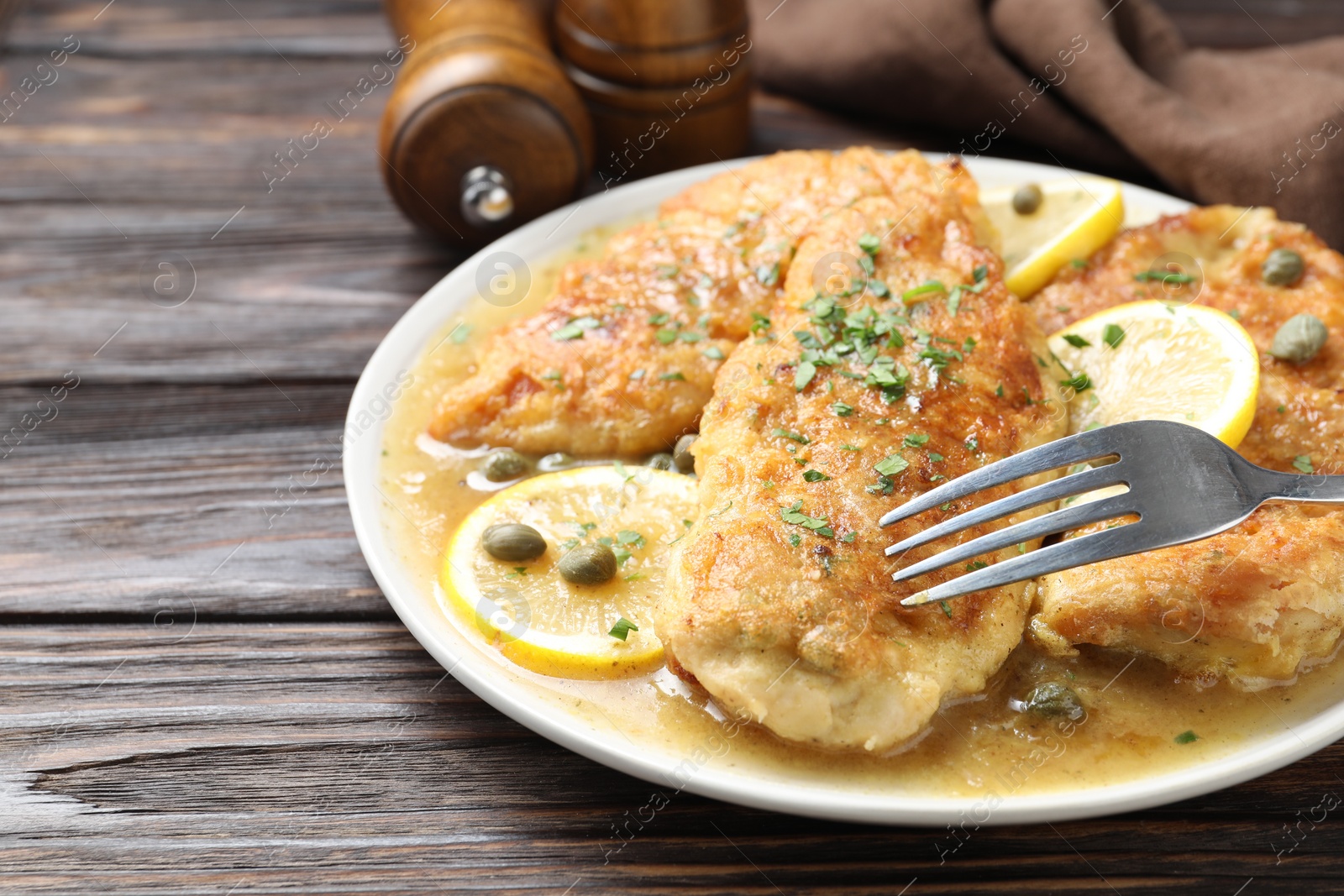 Photo of Delicious chicken piccata on wooden table, closeup