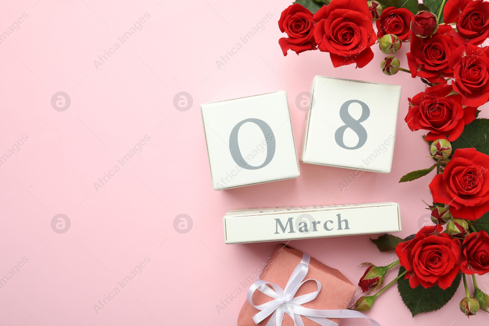 Photo of Wooden block calendar with date 8th of March, gift and roses on pink background, flat lay. Space for text