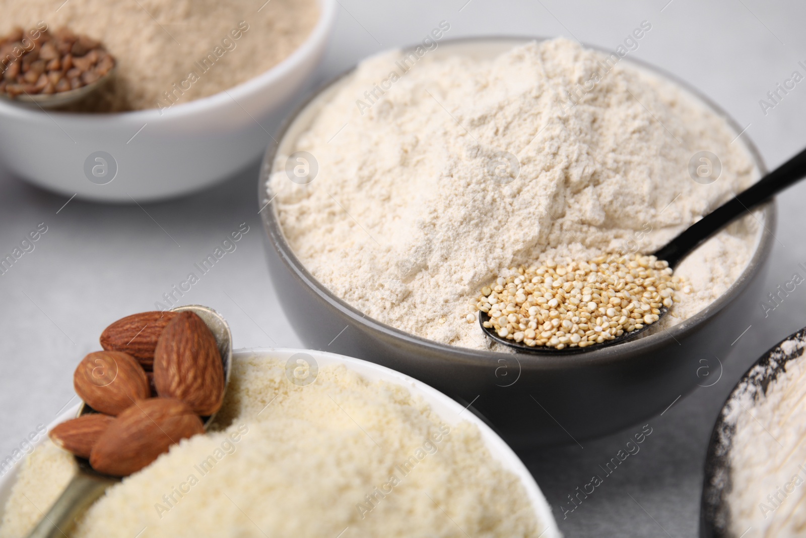 Photo of Bowls with different types of flour and ingredients on light grey table, closeup