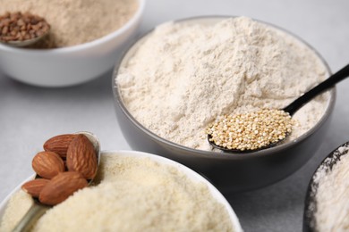 Photo of Bowls with different types of flour and ingredients on light grey table, closeup