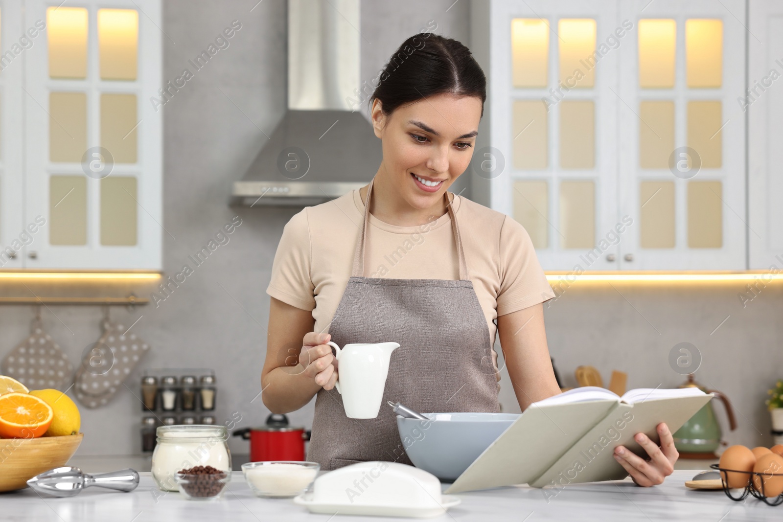 Photo of Young woman with recipe book cooking in kitchen