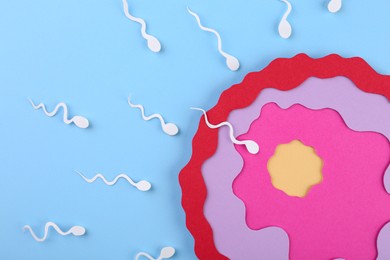 Photo of Fertilization concept. Sperm cells swimming towards egg cell on light blue background, top view
