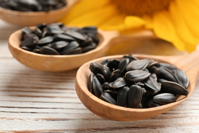 Photo of Spoons with sunflower seeds on wooden table, closeup