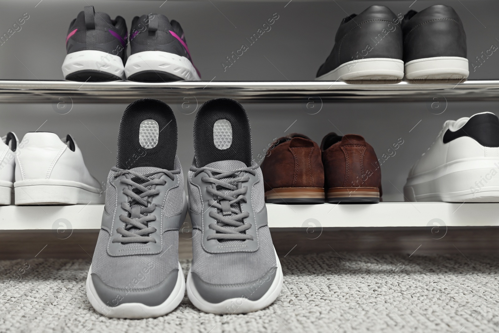 Photo of Orthopedic insoles in shoes on rug near rack