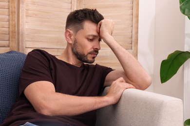 Photo of Upset man sulking on sofa at home. Loneliness concept