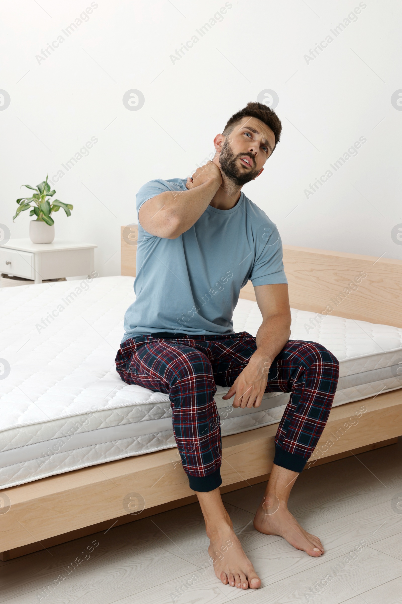 Photo of Man suffering from neck pain after sleeping on uncomfortable mattress at home