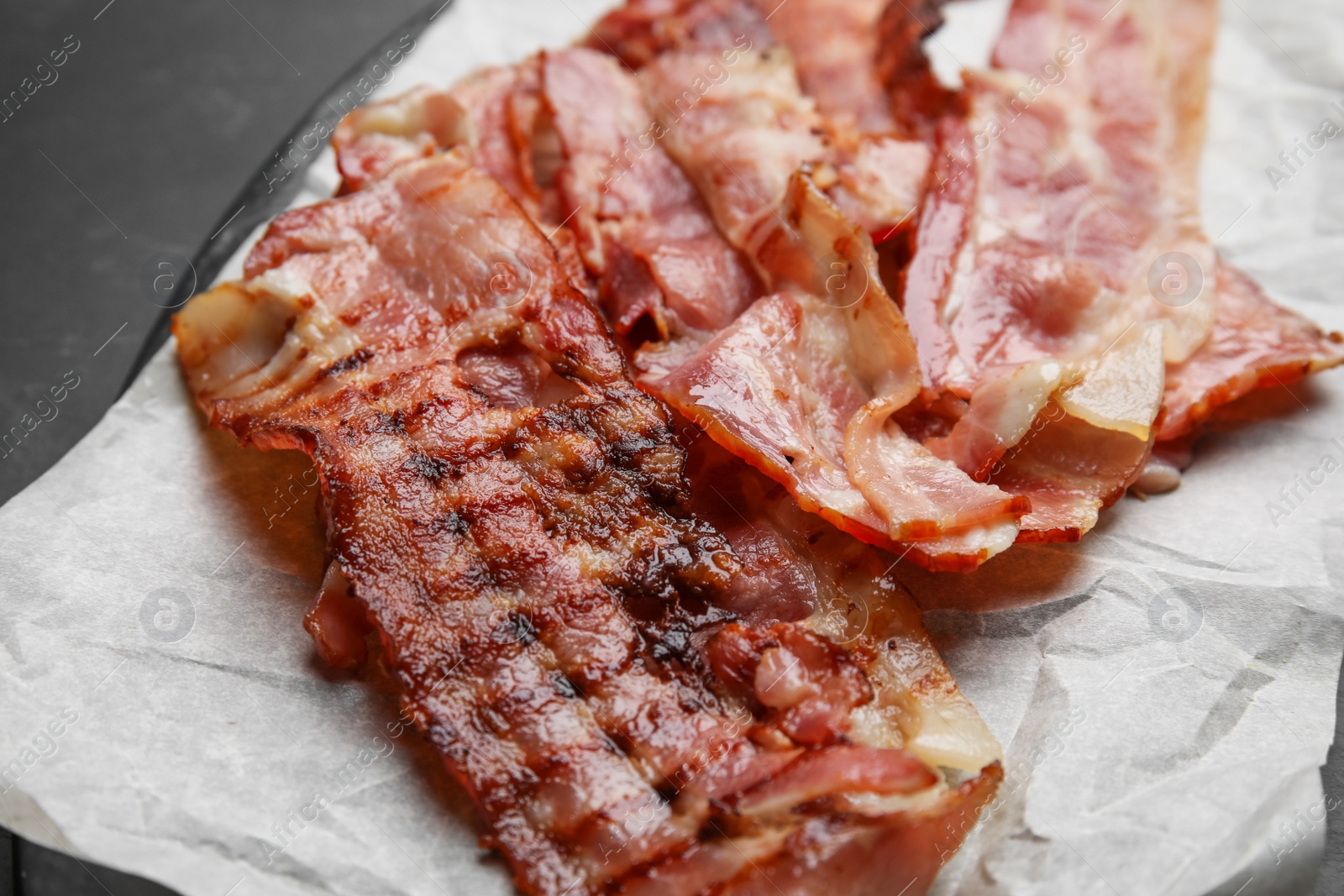 Photo of Slices of tasty fried bacon on dark table, closeup