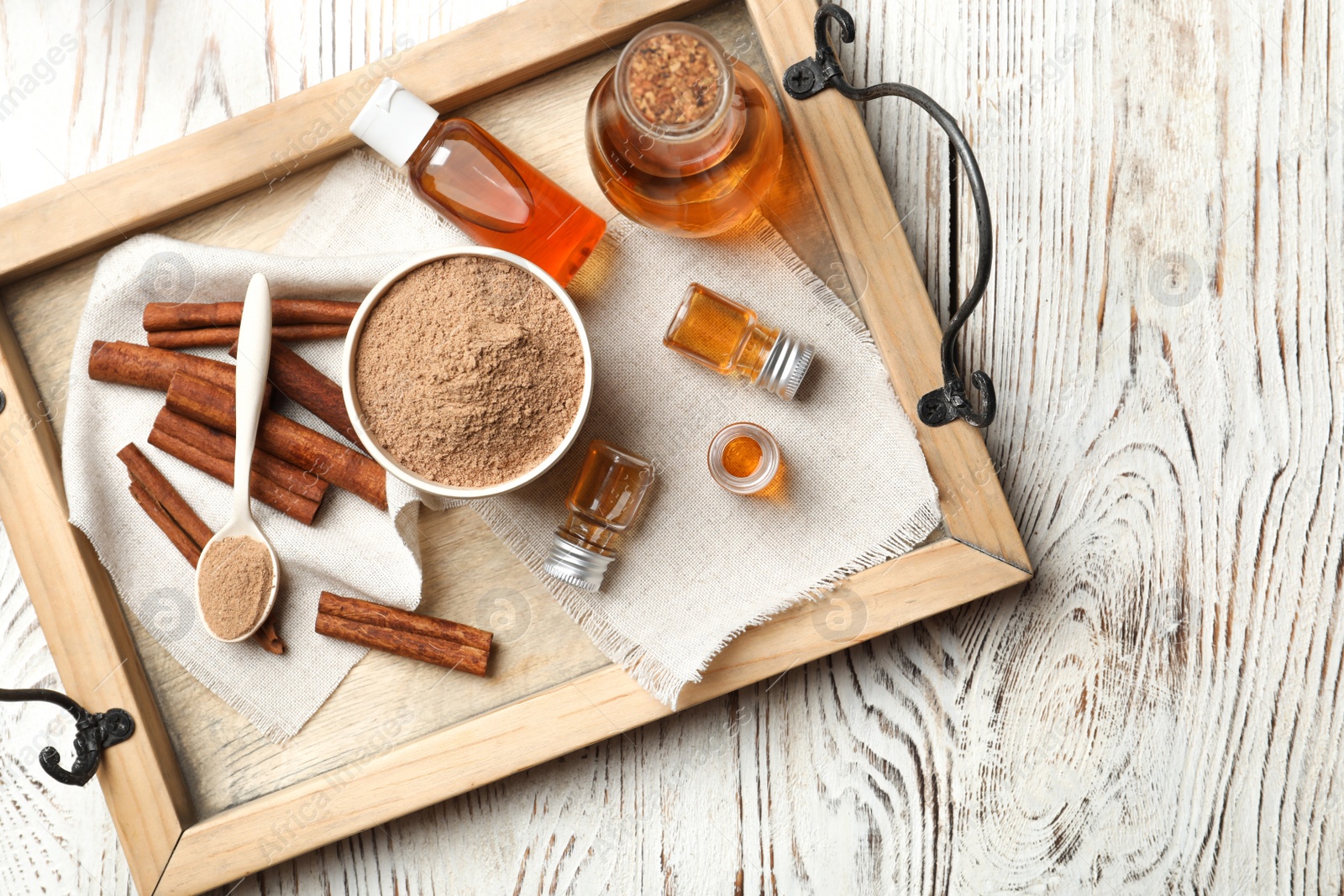 Photo of Bottles with cinnamon oil, powder and sticks on wooden tray