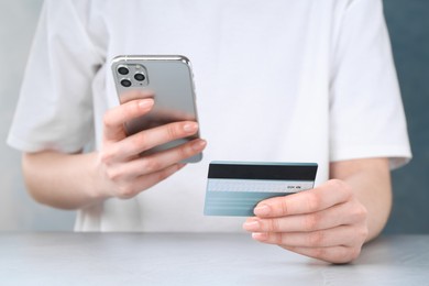 Photo of Online payment. Woman with smartphone and credit card at white table, closeup