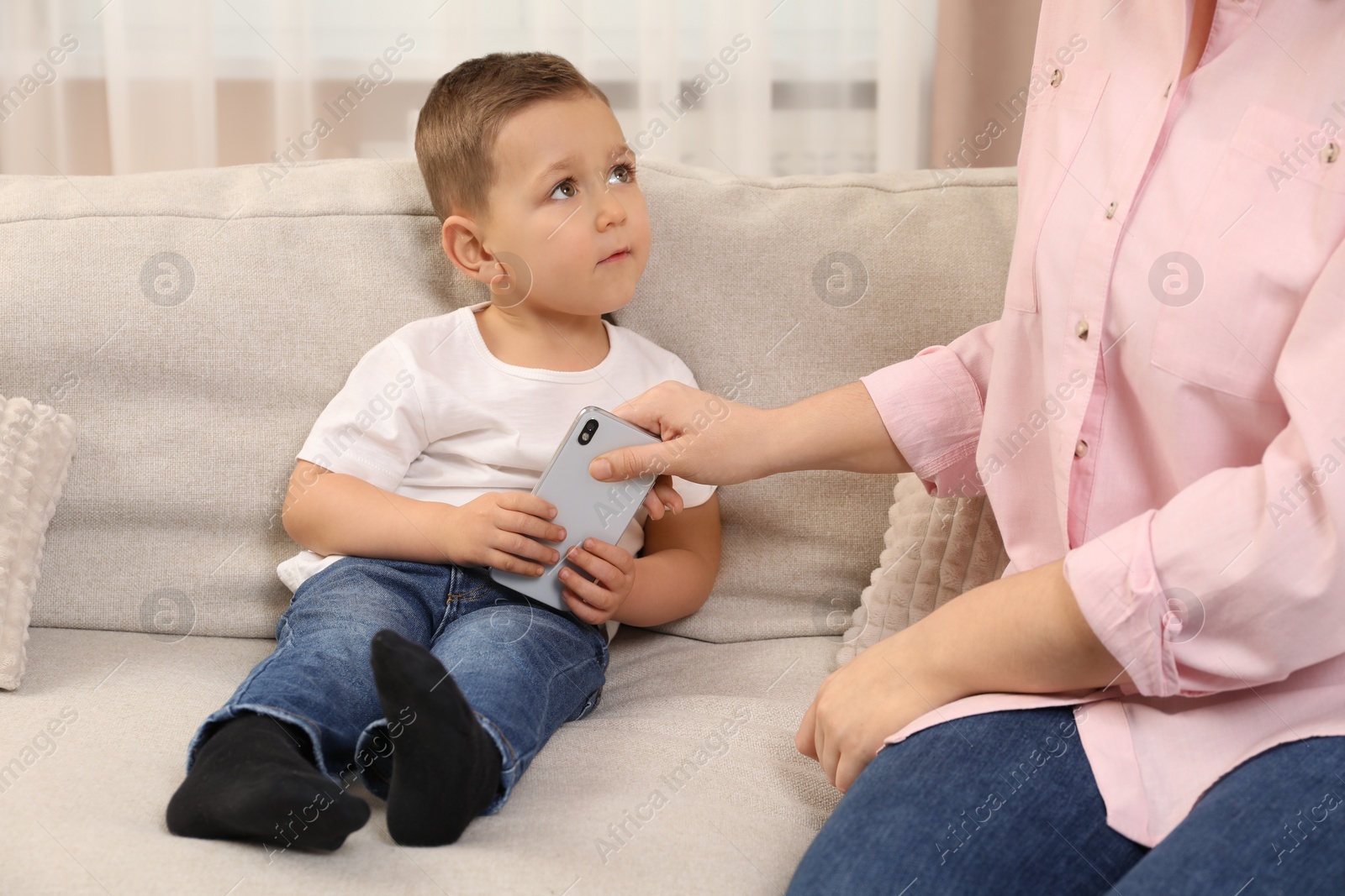 Photo of Internet addiction. Mother taking away smartphone from her little son on sofa at home, closeup