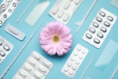 Many gynecological pills, tools and gerbera flower on light blue background, flat lay