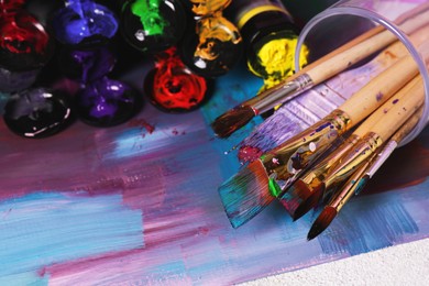 Canvas with colorful abstract painting and different brushes, closeup