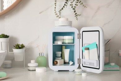 Photo of Cosmetics refrigerator and skin care products on white table indoors