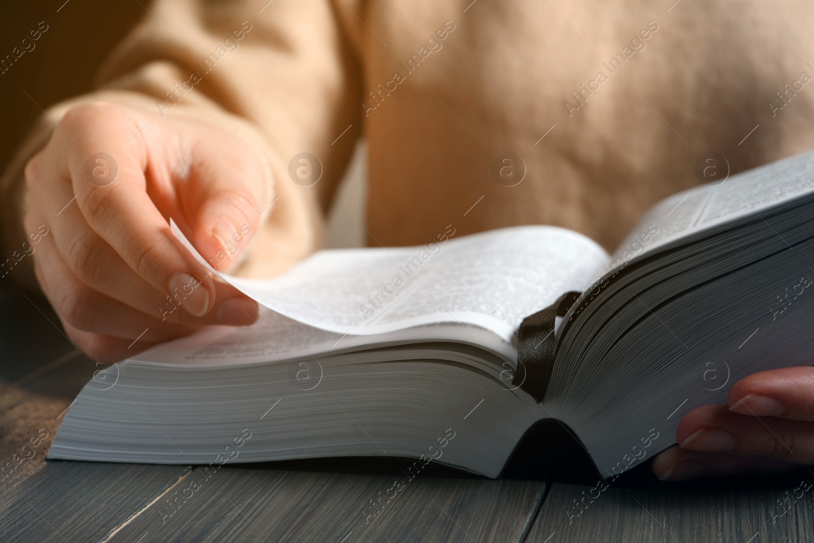 Photo of Woman reading Bible at wooden table, closeup