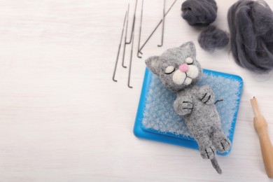 Photo of Felted cat, wool and different tools on light wooden table, flat lay. Space for text