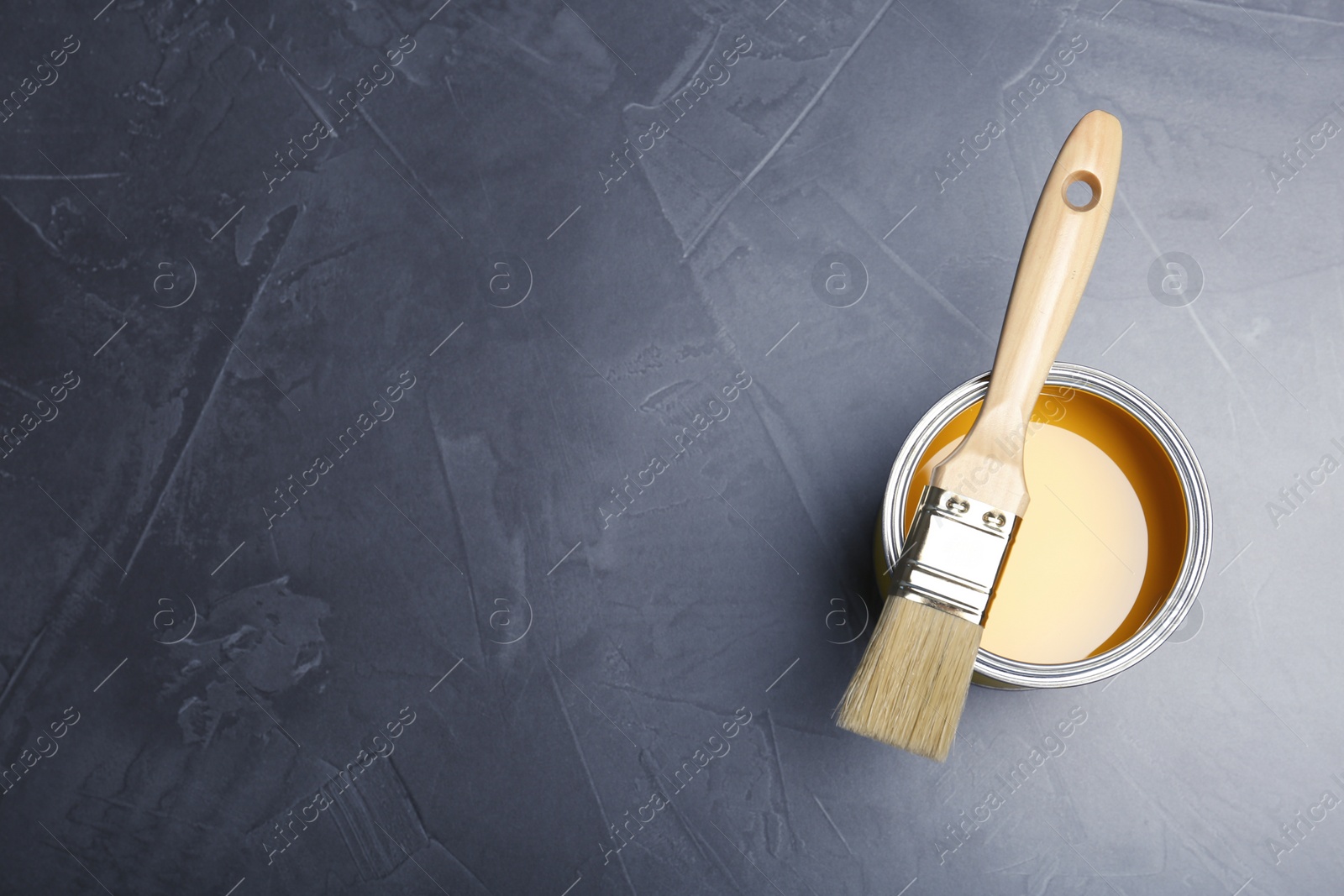 Photo of Can with yellow paint and brush on gray background, top view. Space for text