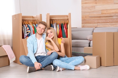 Photo of Happy young couple sitting near wardrobe boxes indoors