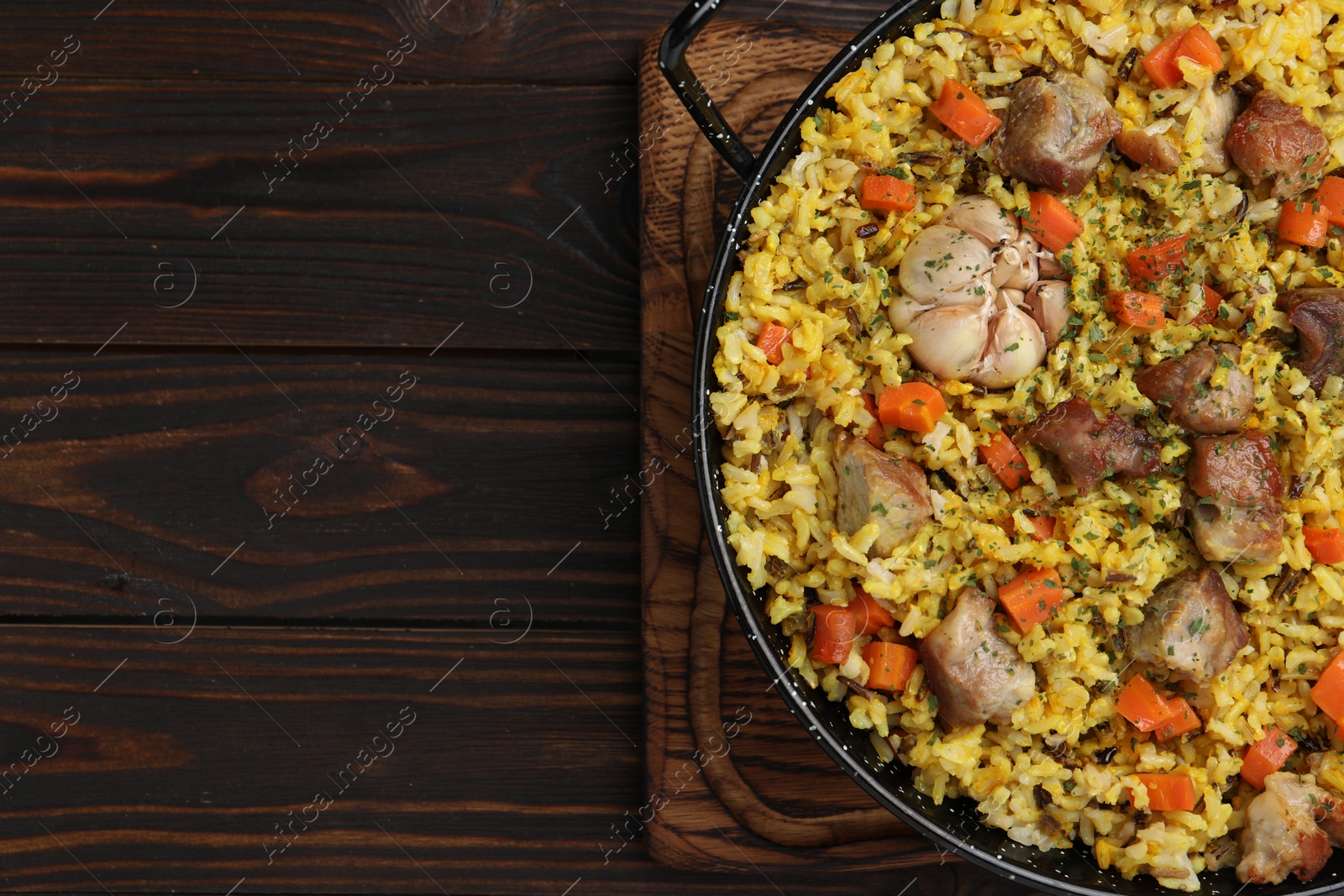 Photo of Delicious pilaf with meat, carrot and garlic on wooden table, top view. Space for text