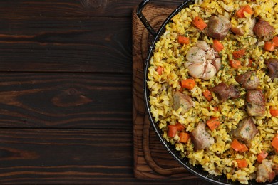 Photo of Delicious pilaf with meat, carrot and garlic on wooden table, top view. Space for text
