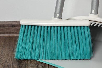 Photo of Plastic broom with dustpan on wooden floor indoors, closeup