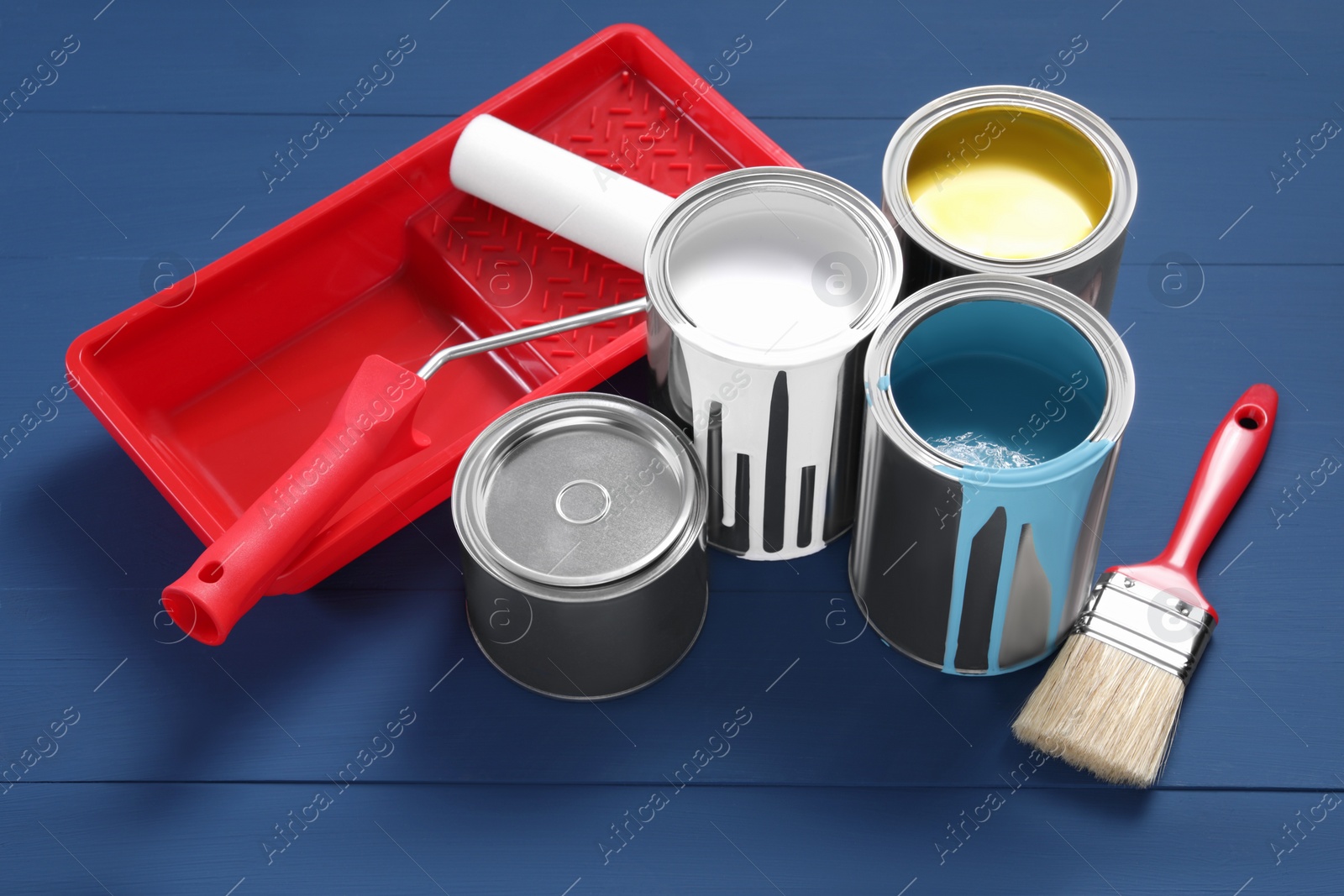 Photo of Cans of paints, brush, roller and tray on blue wooden table