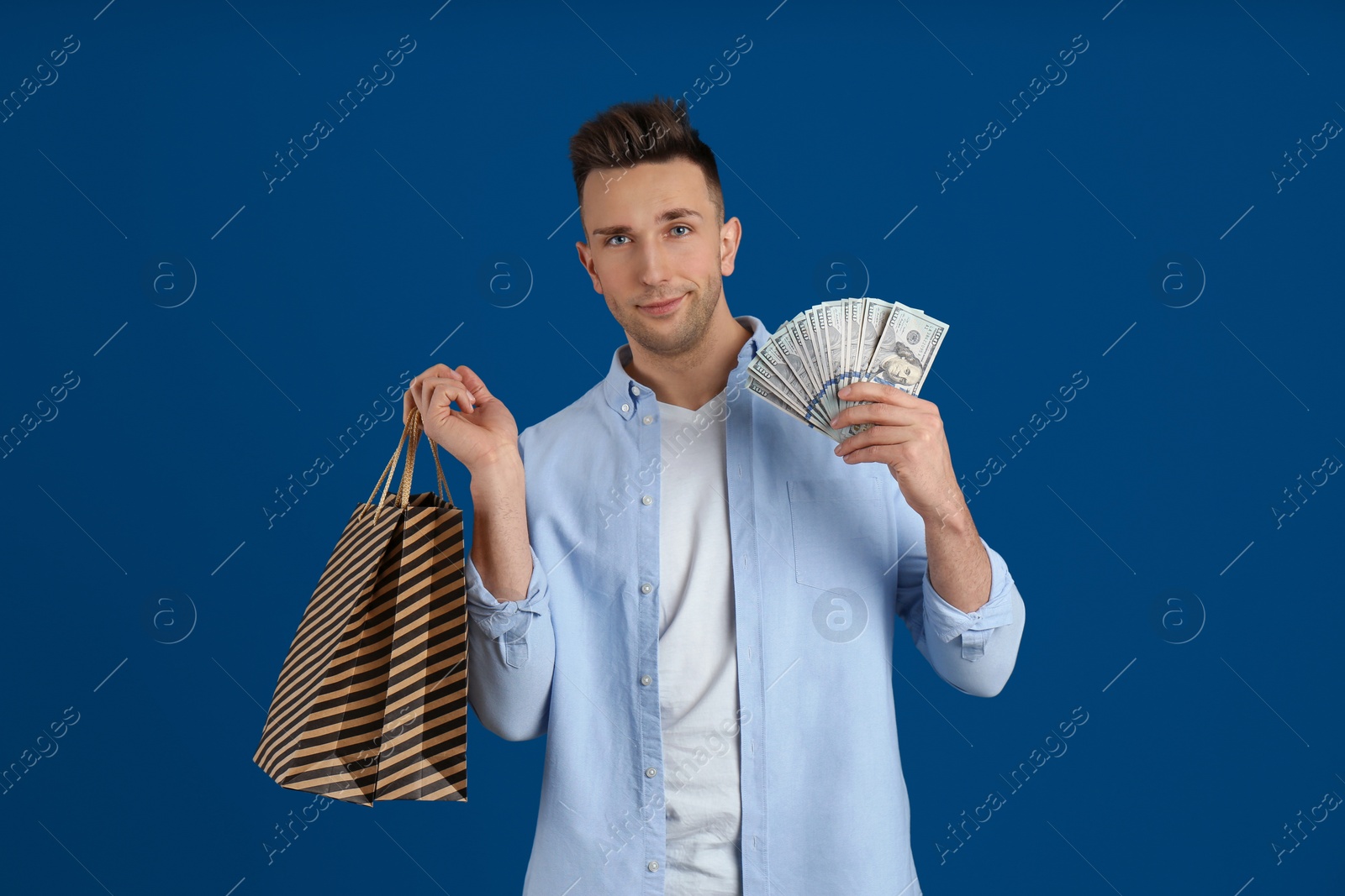 Photo of Happy man with cash money and shopping bags on blue background