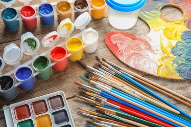 Photo of Different brushes, paints and palette on wooden background