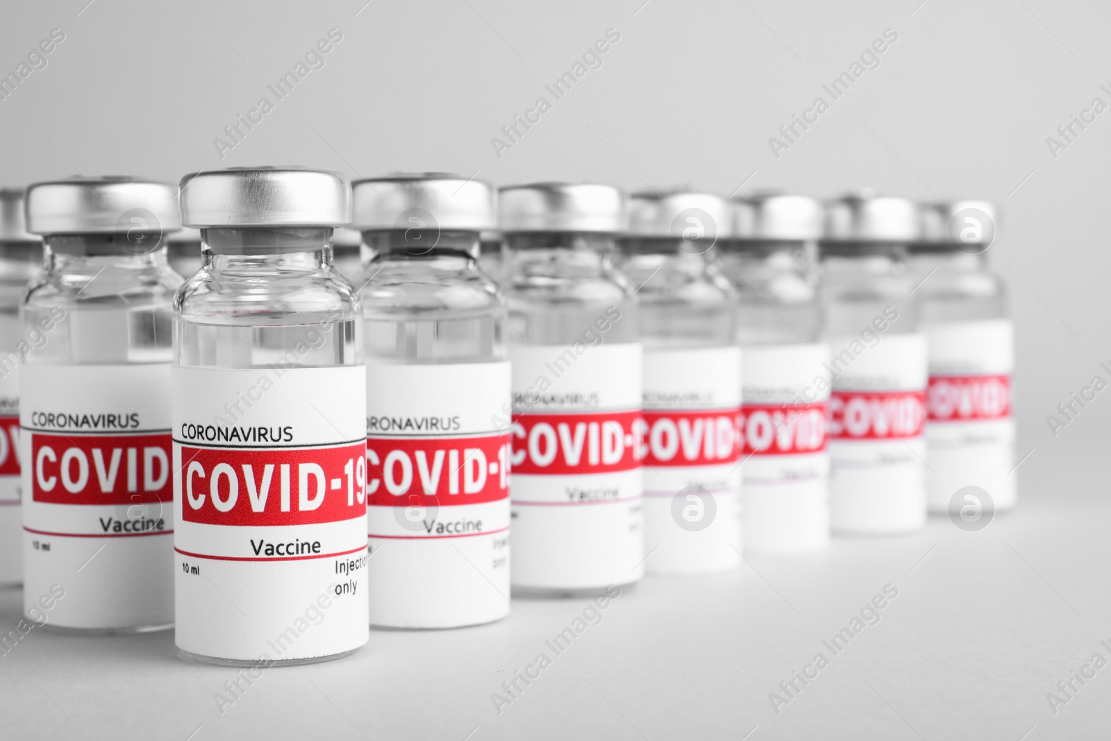 Photo of Glass vials with COVID-19 vaccine on light grey background