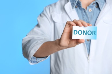 Doctor holding card with word DONOR on light blue background, closeup