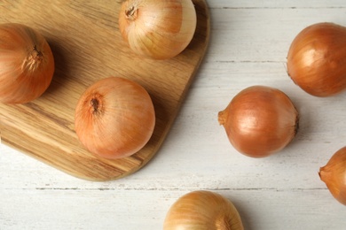 Photo of Ripe onions on white wooden table, flat lay
