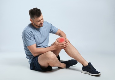 Full length portrait of man with knee problems sitting on grey background