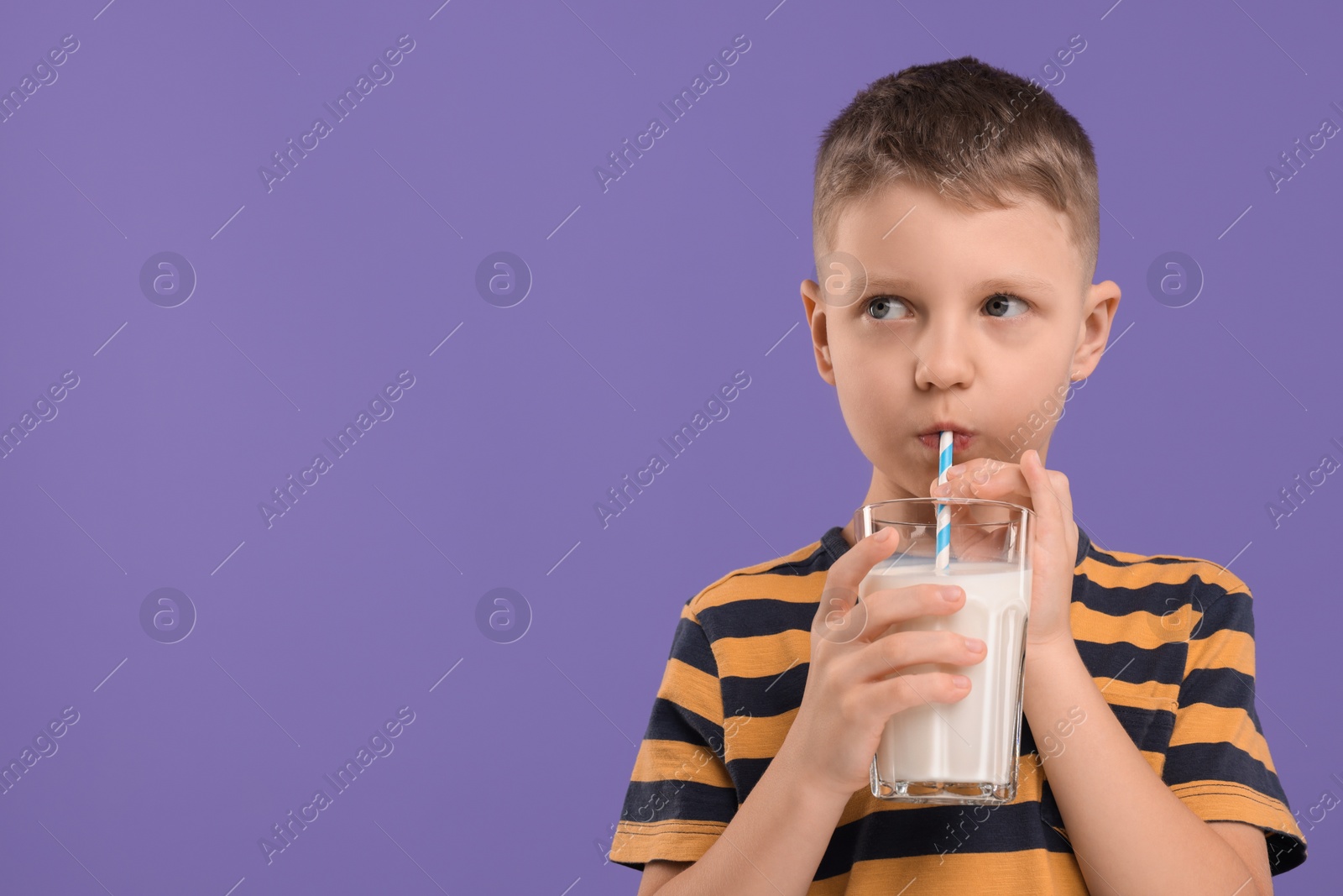 Photo of Cute boy drinking fresh milk from glass on violet background, space for text