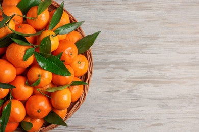 Photo of Fresh ripe juicy tangerines and green leaves on white wooden table, top view. Space for text