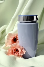 Photo of Bottle of hair care cosmetic product and beautiful flowers on light green fabric
