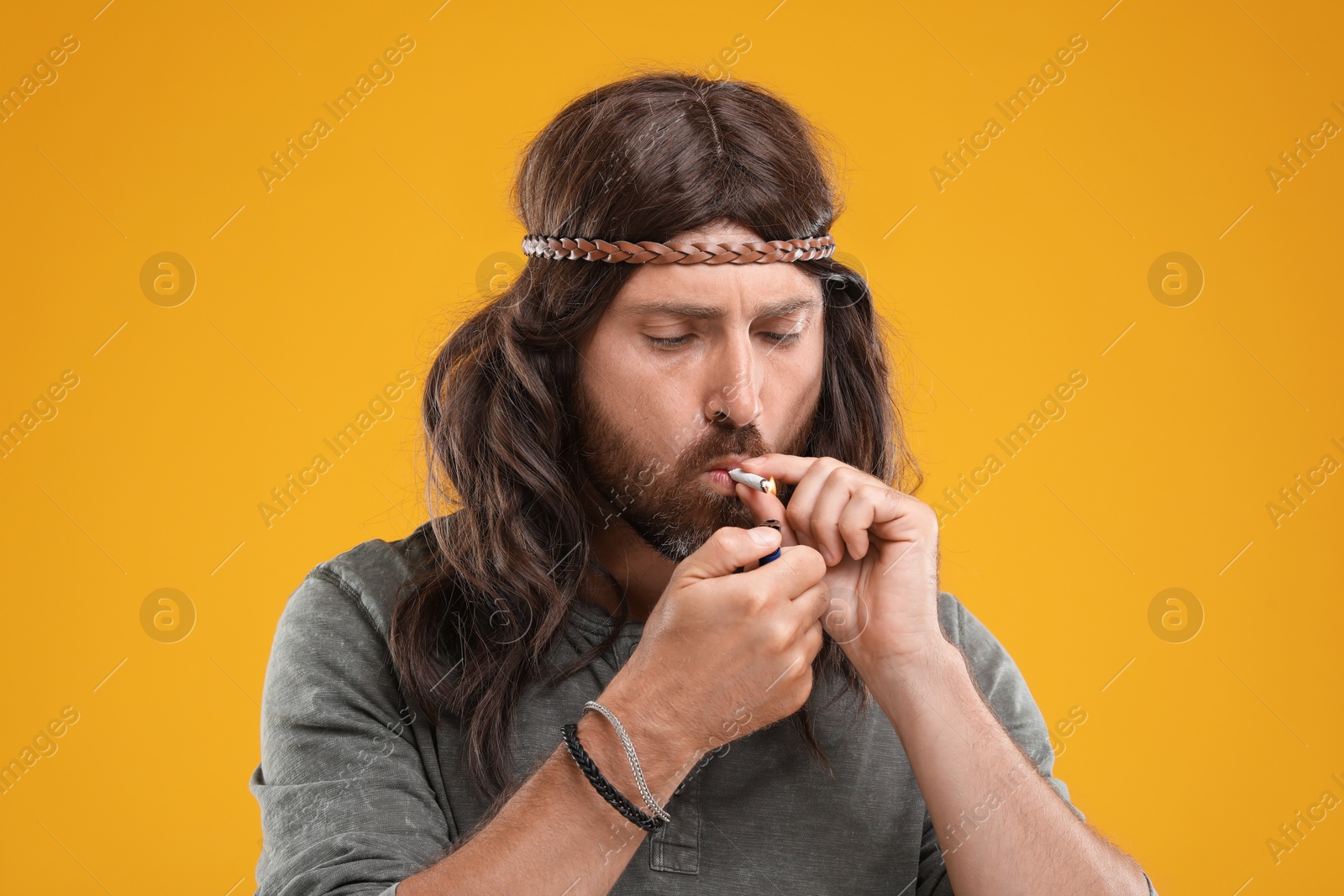 Photo of Hippie man lighting cigarette on orange background