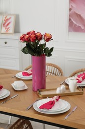 Photo of Color accent table setting. Plates, cutlery, pink napkins and vase with beautiful roses in dining room