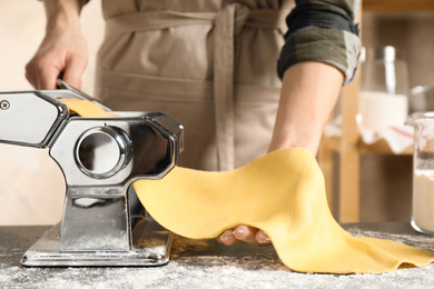 Woman preparing dough with pasta maker machine at table, closeup