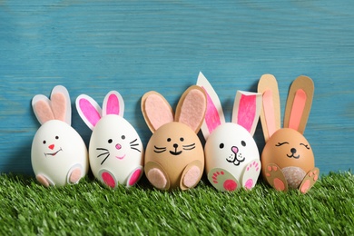 Easter eggs as cute bunnies on green grass against light blue wooden background