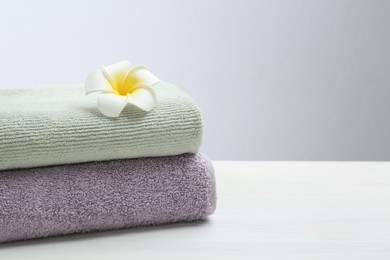 Different folded towels and plumeria flower on white wooden table, closeup. Space for text