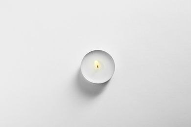 Photo of Burning wax candle on white background, top view