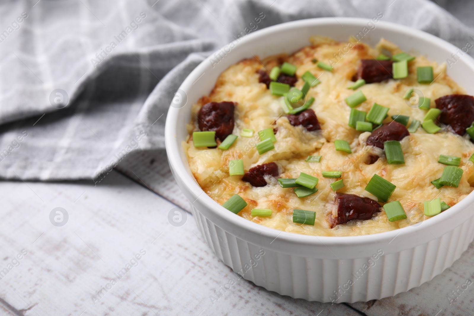 Photo of Tasty sausage casserole with green onion in baking dish on white wooden table, closeup. Space for text