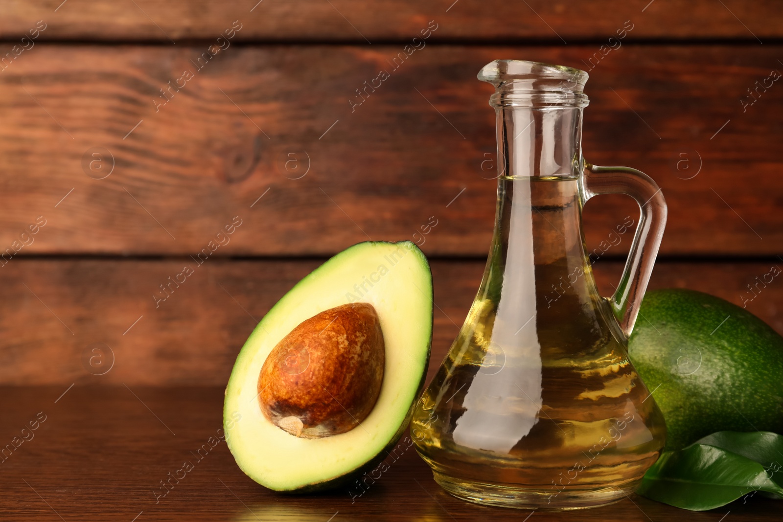 Photo of Glass jug of cooking oil and fresh avocados on wooden table, space for text