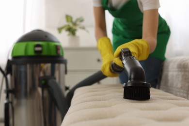 Photo of Professional janitor in uniform vacuuming furniture indoors, closeup