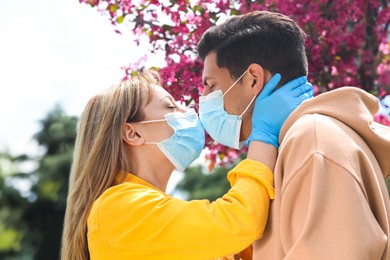Photo of Couple in medical masks and gloves trying to kiss outdoors