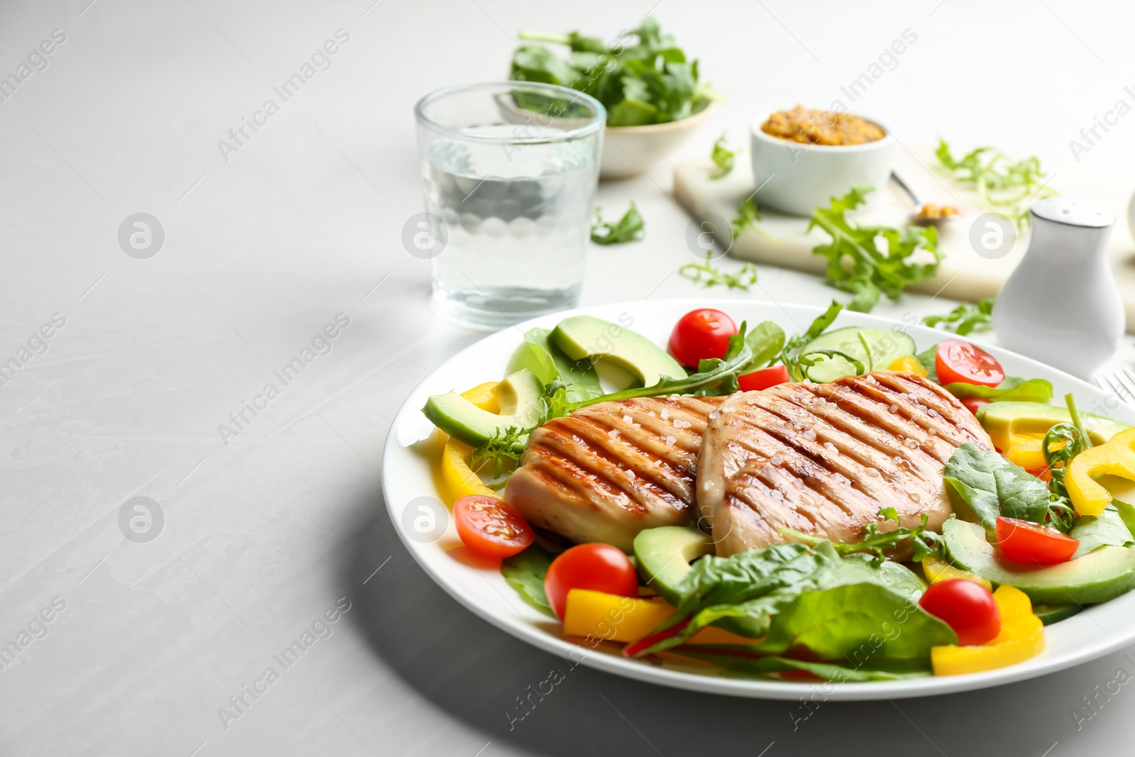 Photo of Tasty grilled chicken fillets with vegetables on light grey table. Space for text