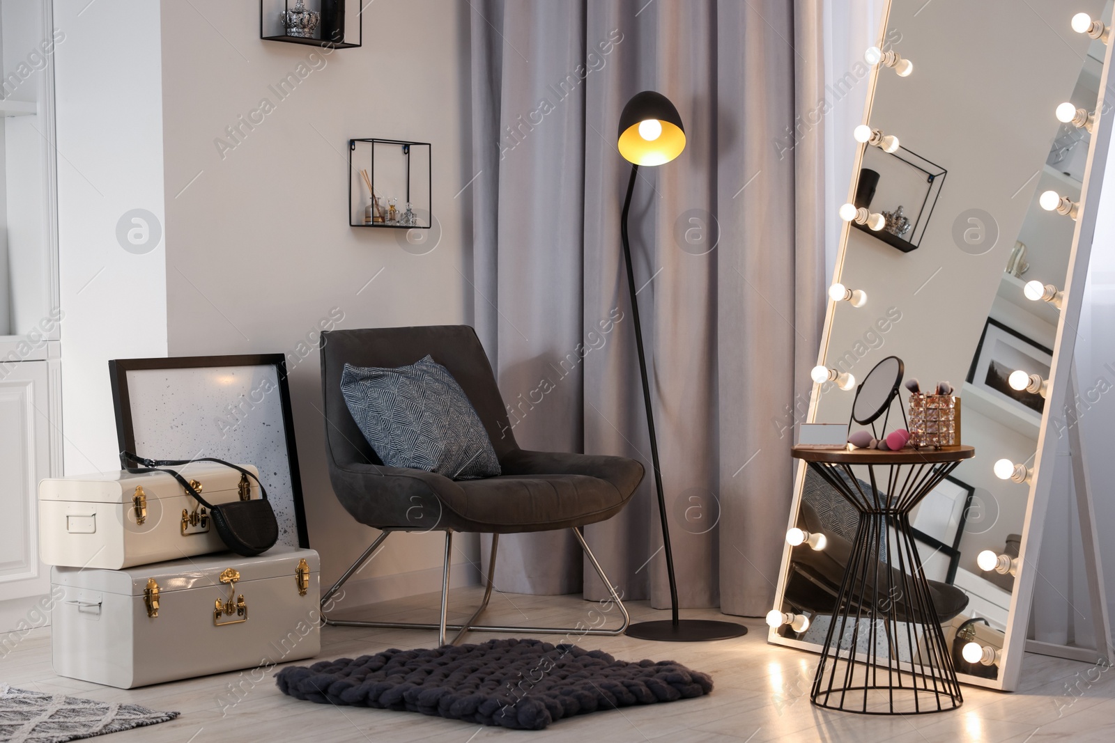 Photo of Makeup room. Stylish mirror with light bulbs, beauty products on table and armchair indoors