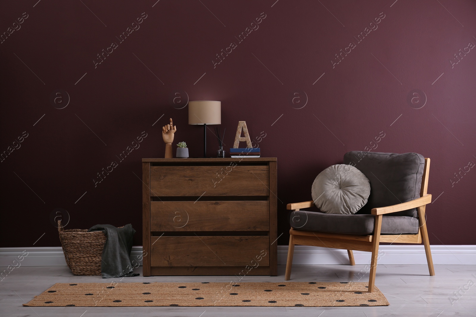 Photo of Elegant room interior with stylish chest of drawers and comfortable armchair near brown wall