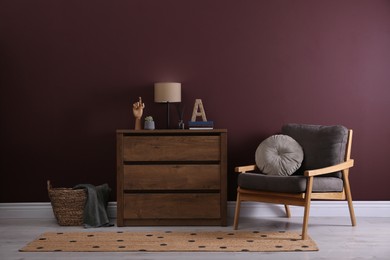 Elegant room interior with stylish chest of drawers and comfortable armchair near brown wall
