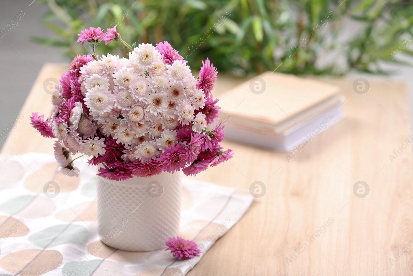 Photo of Vase with beautiful bouquet, books and cloth on wooden table, space for text